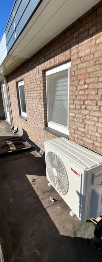 Airco buitenunit op een dakterras langs een bakstenen muur